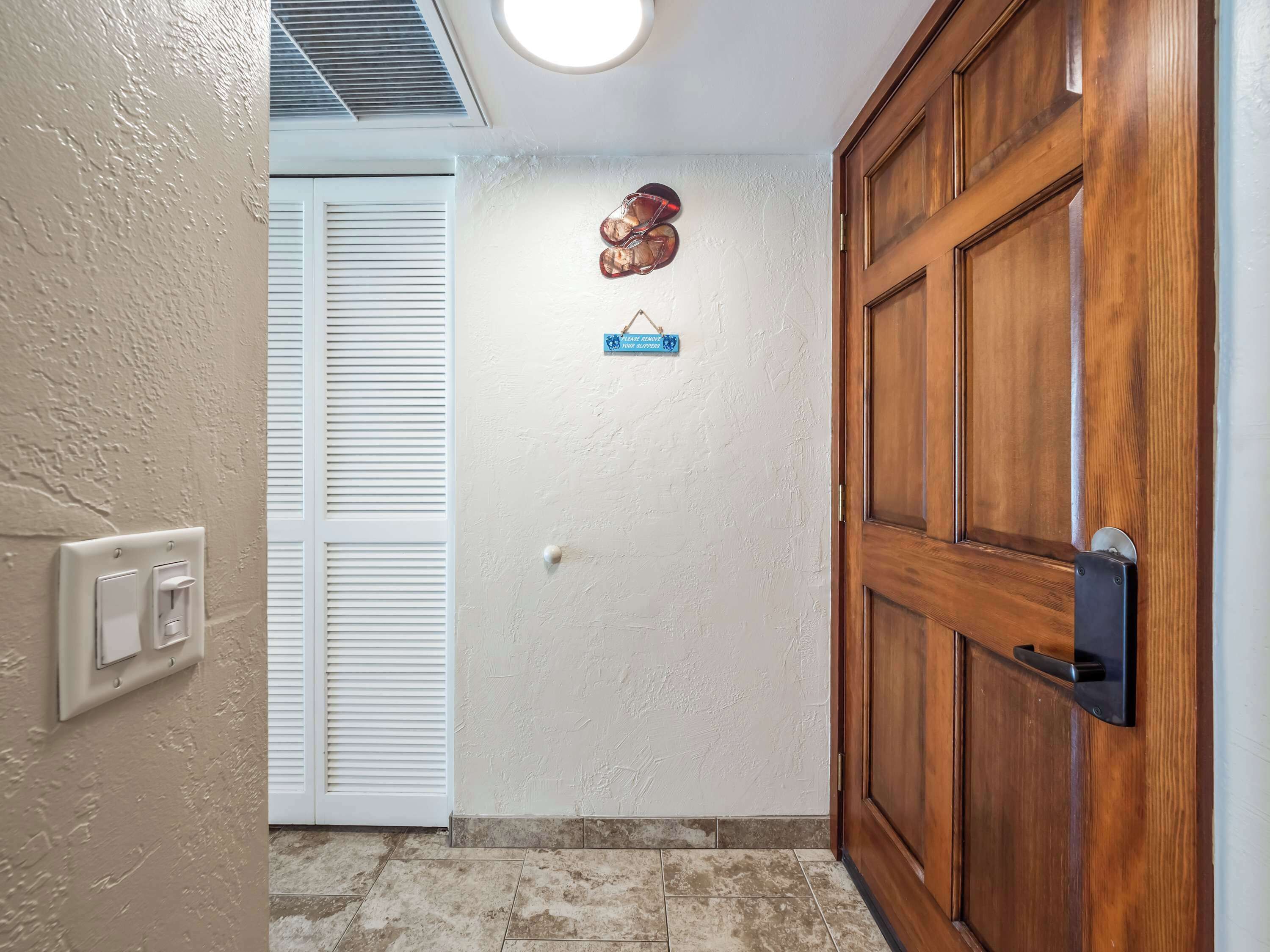A hallway with a wooden door, a white wall, and a ceiling vent.