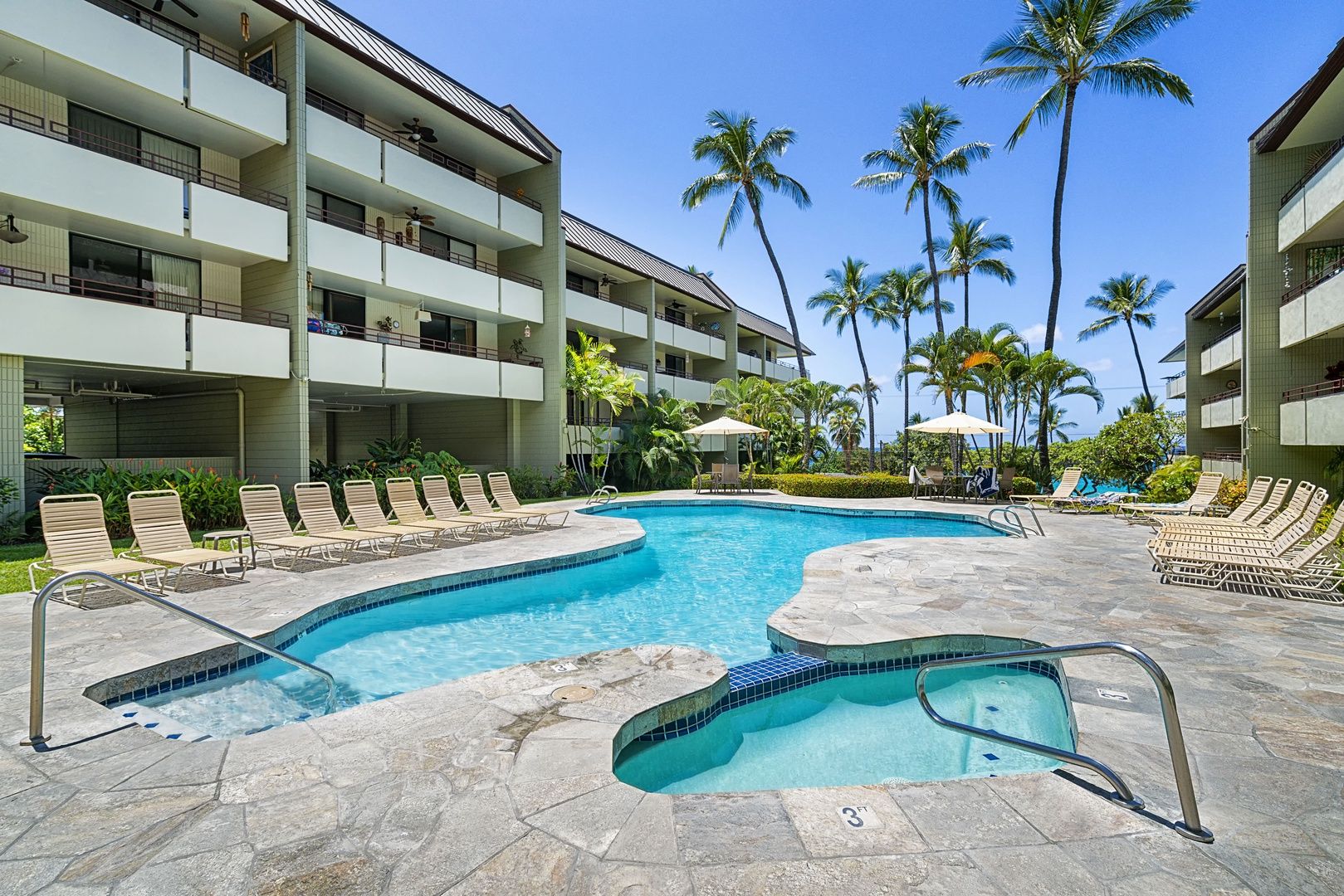 A hotel pool area with multiple lounge chairs and a hot tub.