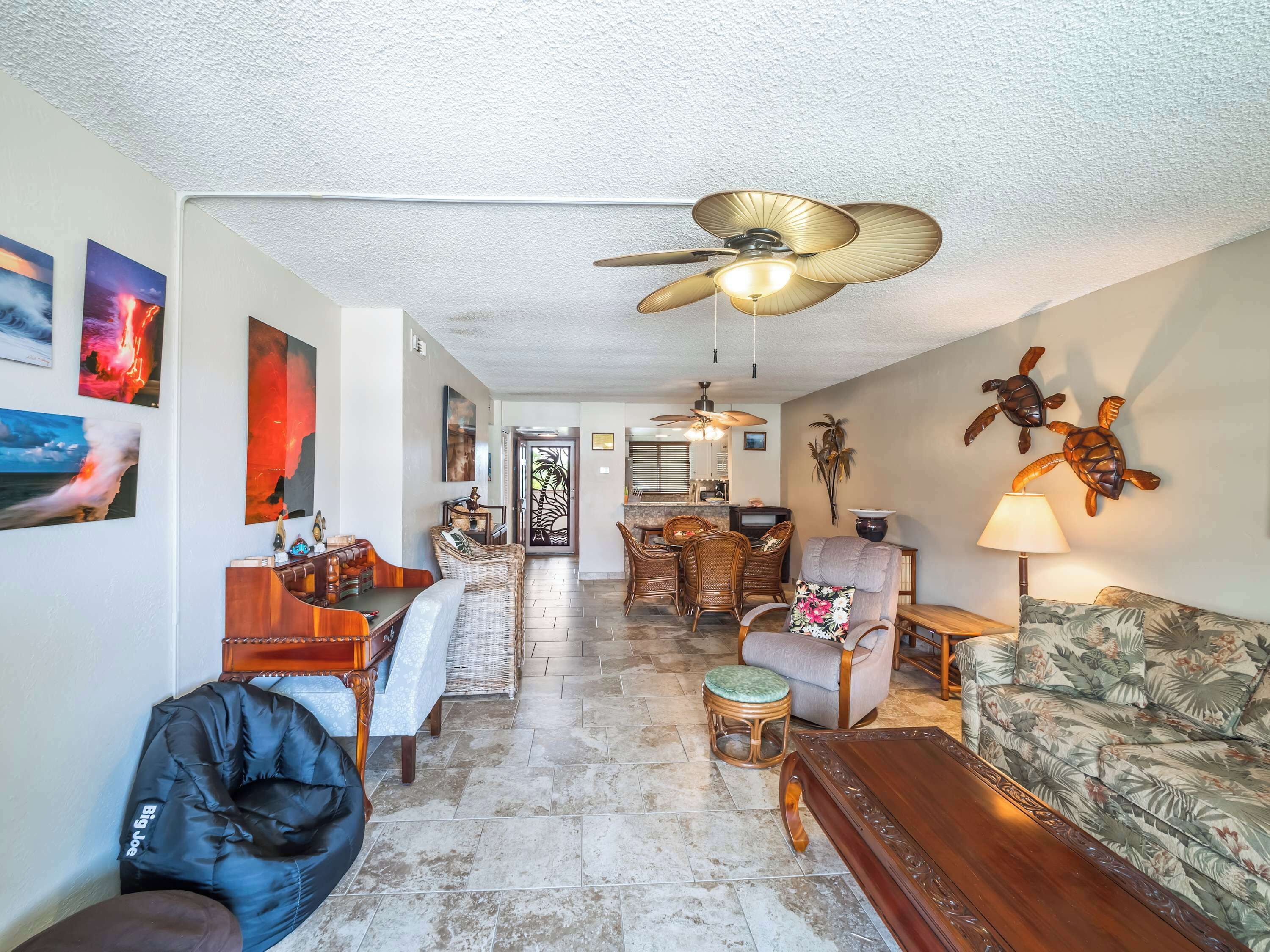 A spacious living room with a ceiling fan, a dining area with wicker furniture, and a kitchen in the background.