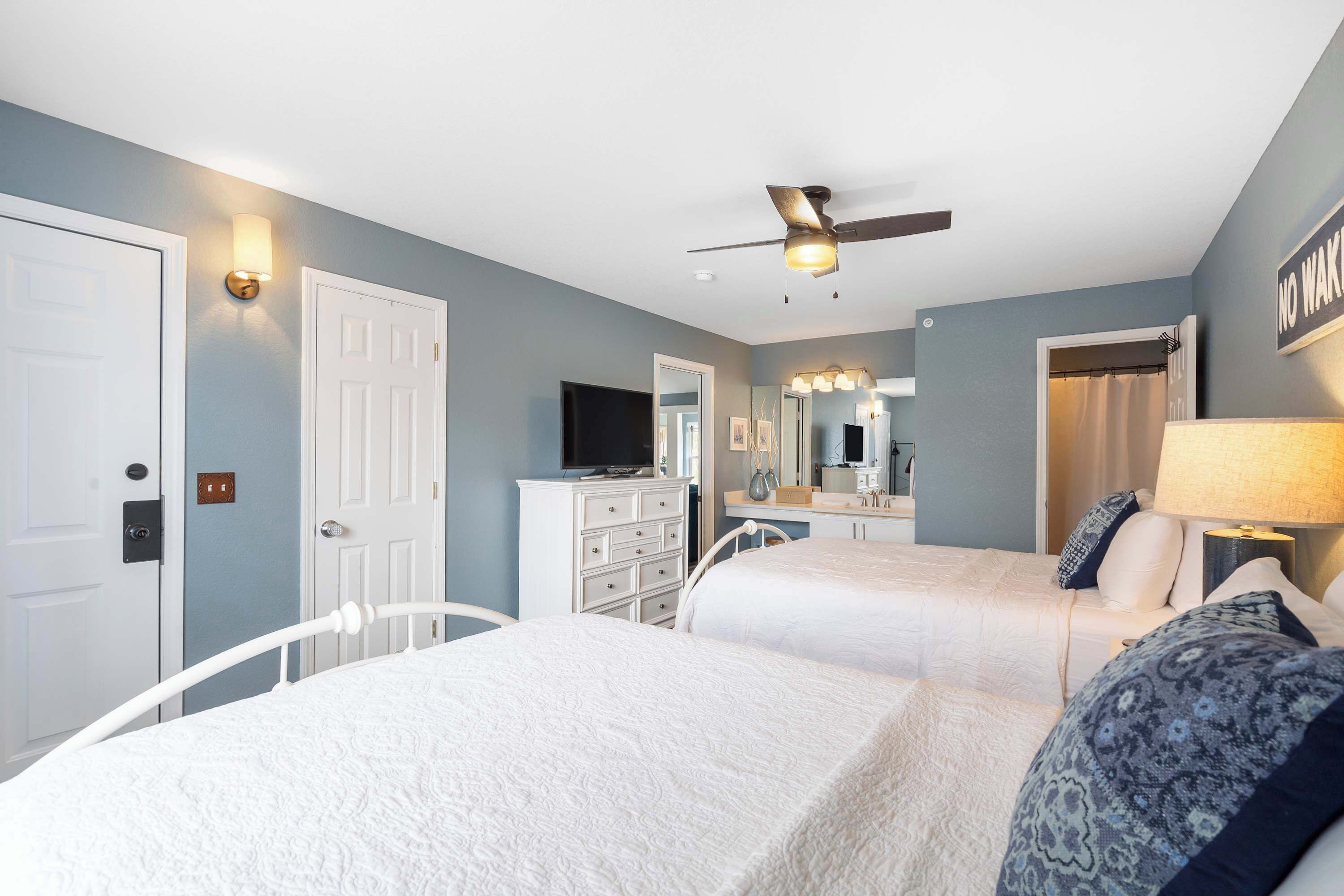 A hotel room with two beds, a ceiling fan, a TV, a dresser, and a mirror.