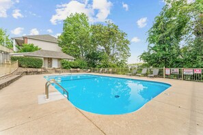 A swimming pool with a metal ladder, surrounded by a fence with warning signs, trees, and a house in the background. - Eagle's Nest at The Club- Chic 2BR Golf View Condo (Branson)