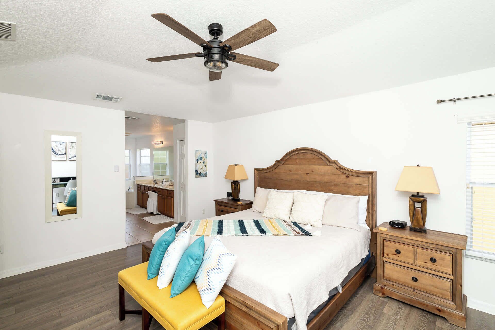 A bedroom with a wooden bed, a bench, a nightstand, a lamp, and a ceiling fan.