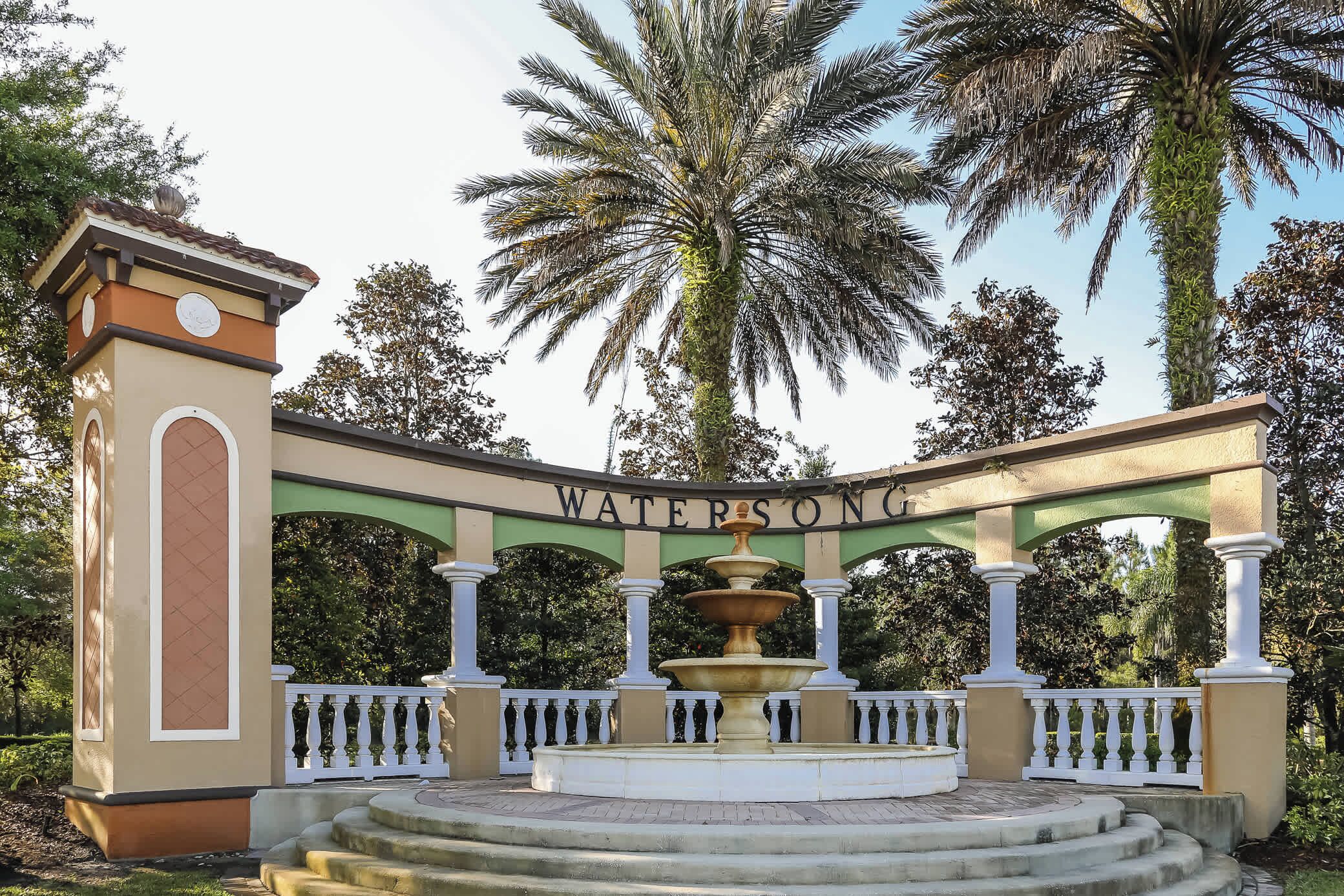 A fountain with a multi-tiered design, surrounded by a white balustrade and a sign reading "WATERSONG."