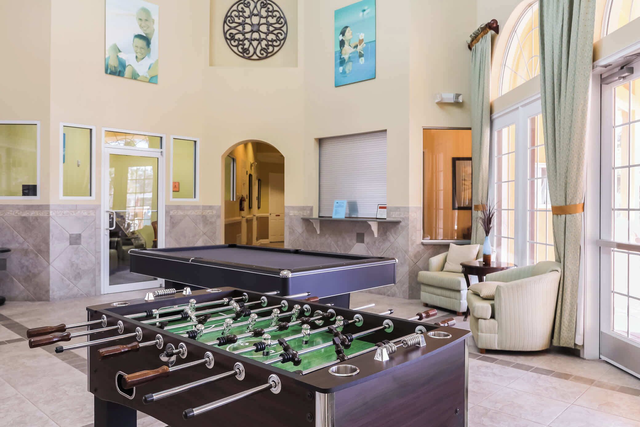 A room with a foosball table, a pool table, and a sofa.