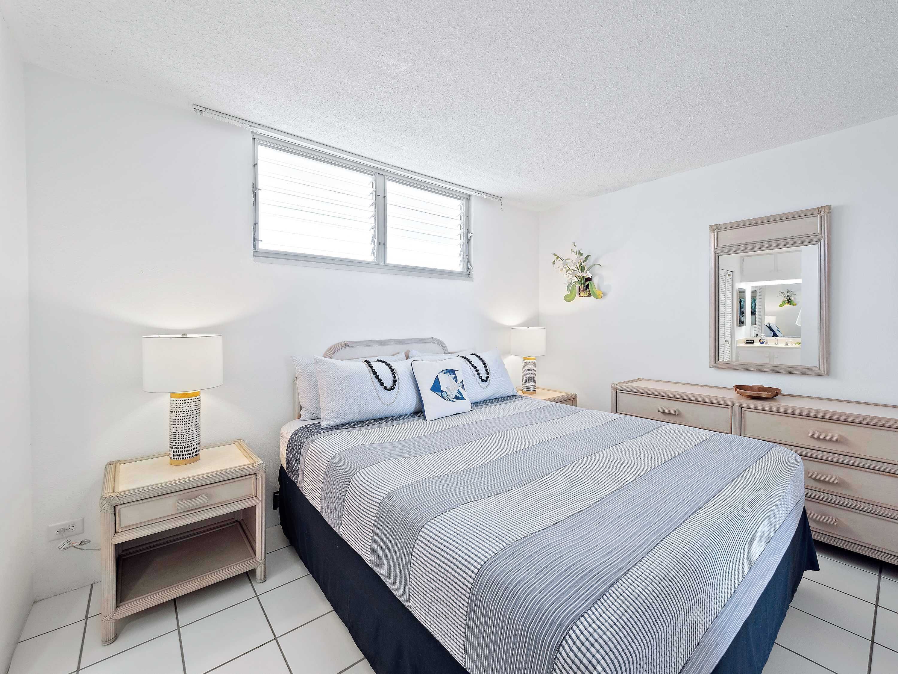 Une chambre à coucher comprenant un lit, des tables de chevet, une commode, un miroir et une fenêtre.