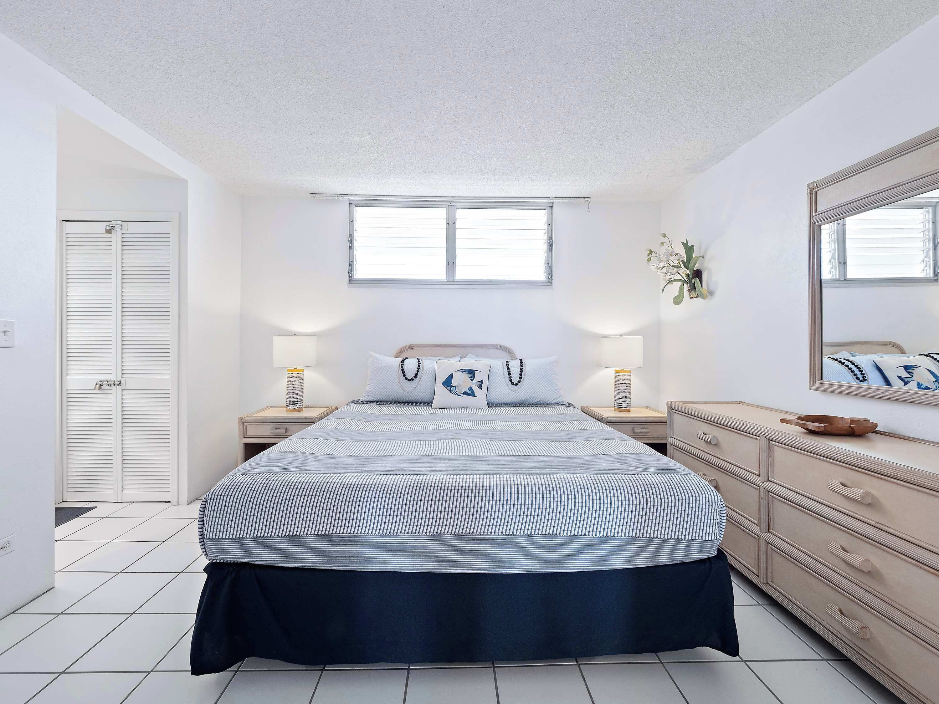 A bedroom with a bed, bedside tables, a dresser, a window, and a door.
