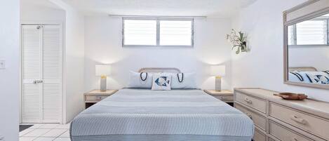 Un dormitorio con cama, mesitas de noche, cómoda, ventana y puerta.