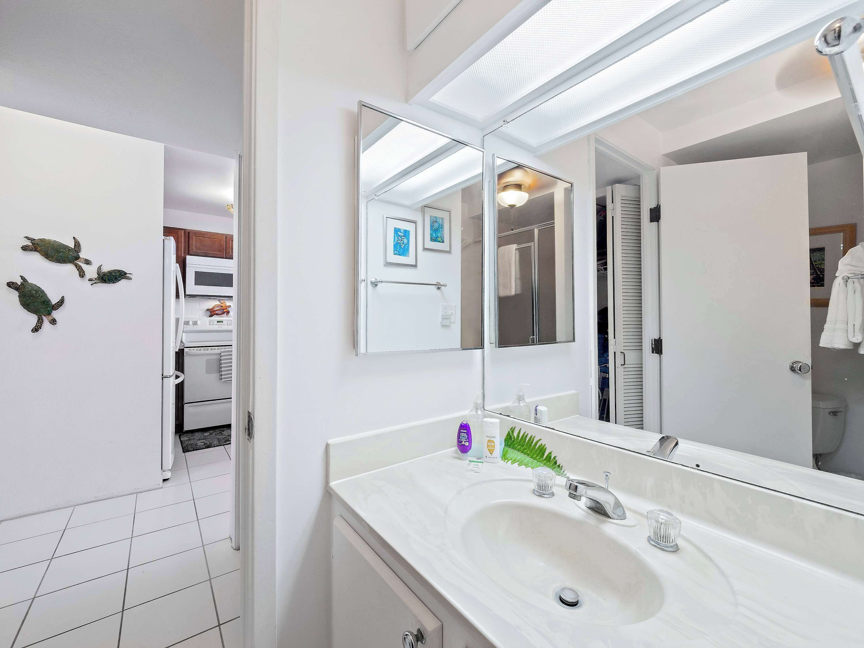 Une salle de bain moderne avec un lavabo blanc, un grand miroir et une douche visible à travers une porte ouverte.