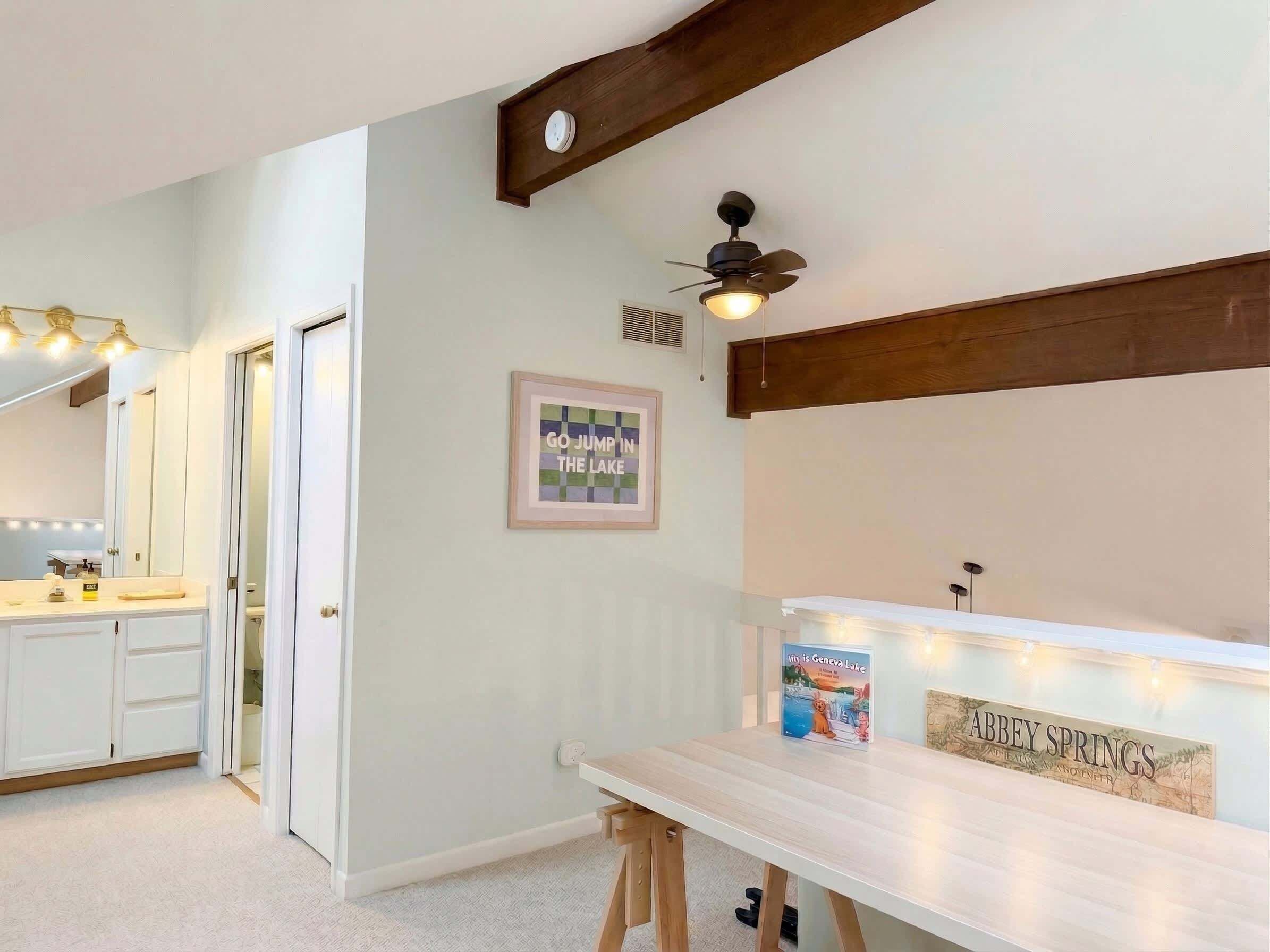 A bathroom with a vanity, a ceiling fan, a framed quote on the wall, and a sign on the counter.