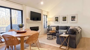 Una sala de estar con chimenea, un conjunto de sofás, una mesa de comedor con sillas y un televisor montado en la pared.
