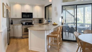 Una cocina moderna con armarios blancos, una isla central y una zona de comedor con sillas de mimbre.