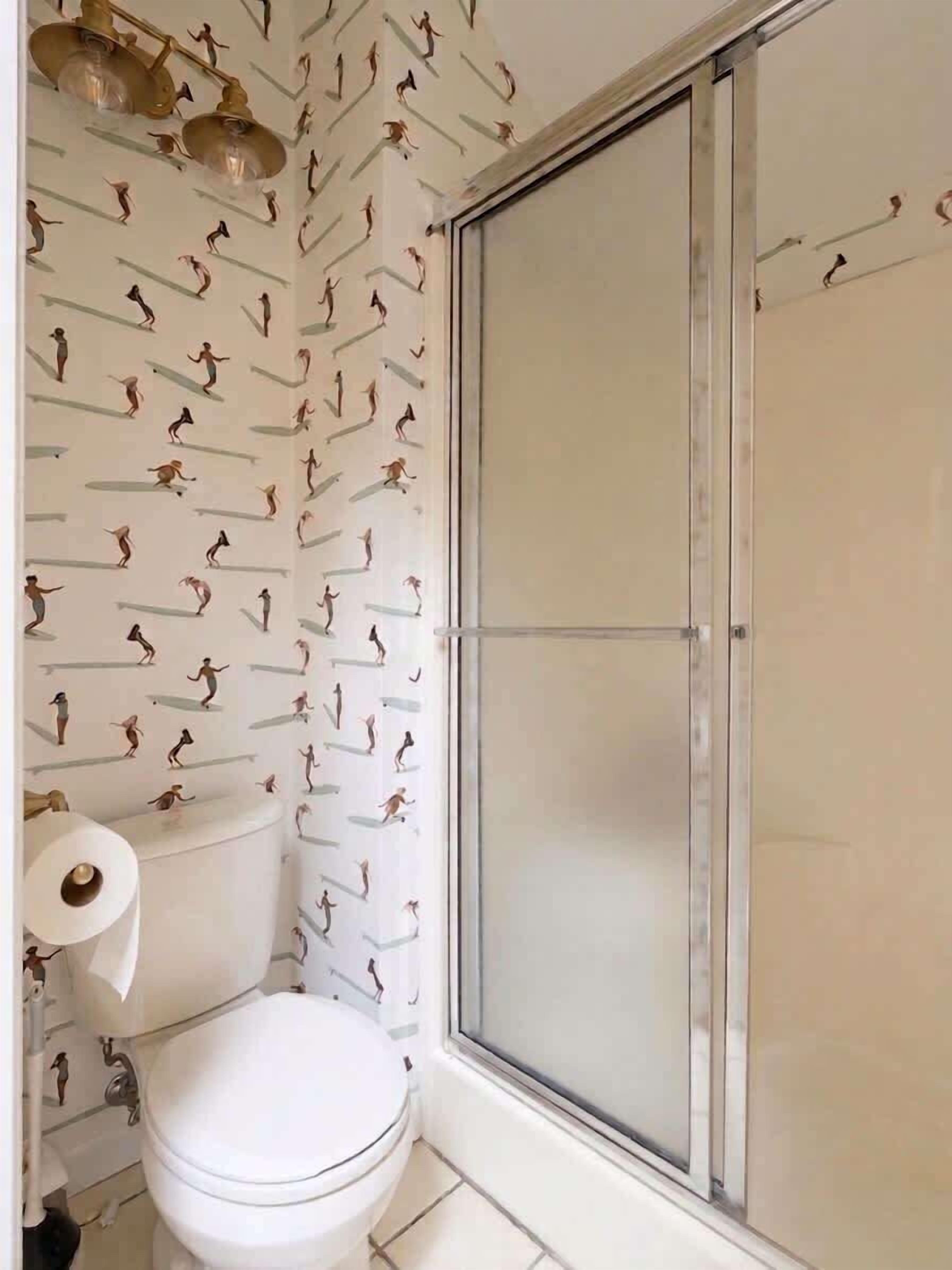 Une salle de bain comprenant des toilettes, une douche et un mur orné d’un motif figuratif.