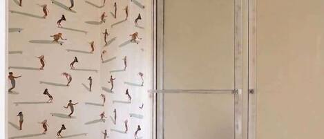 Une salle de bain comprenant des toilettes, une douche et un mur orné d’un motif figuratif.