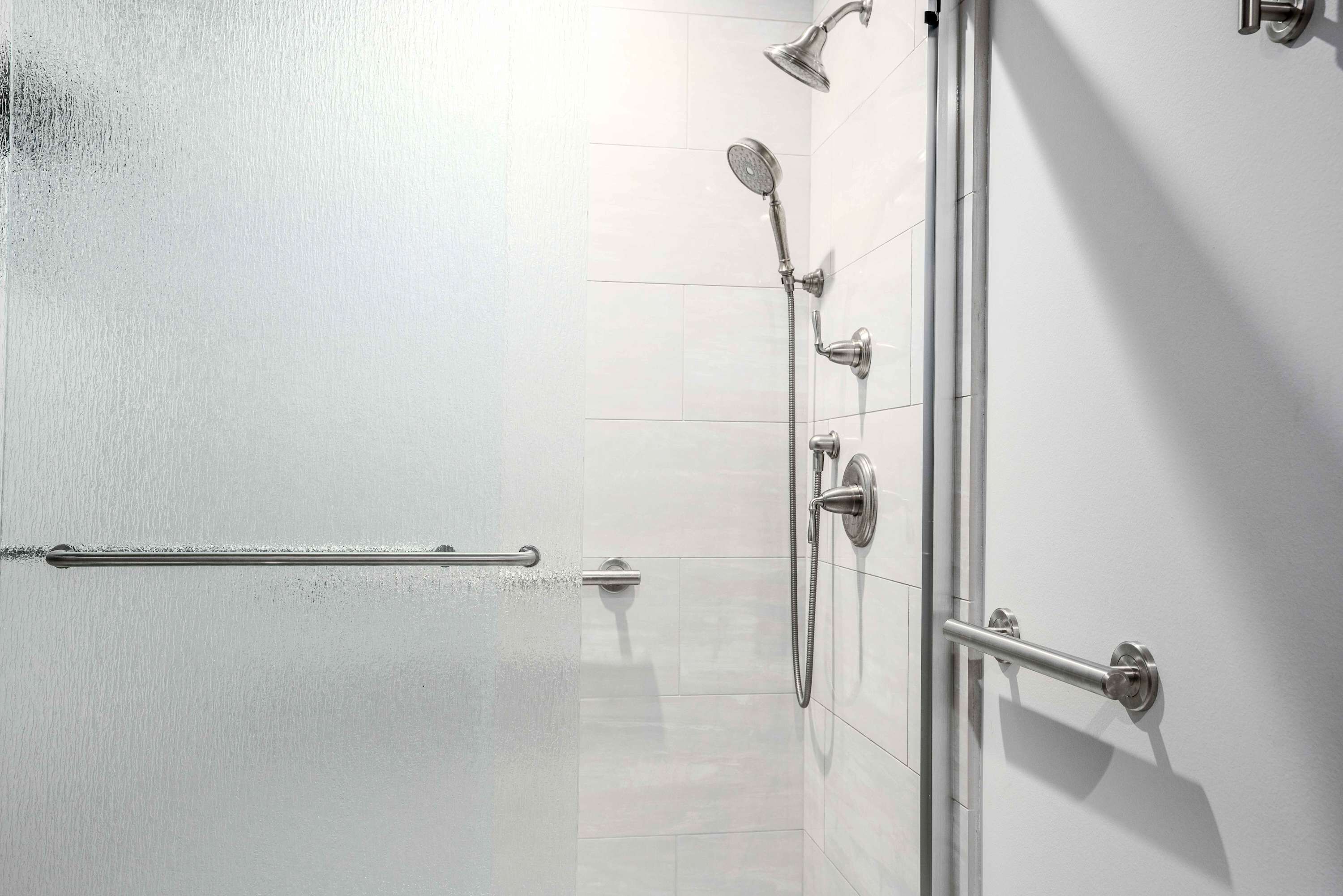 A shower area with a handheld showerhead, a wall-mounted showerhead, and a handheld shower attachment.