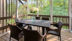 Un patio exterior cubierto con una mesa, sillas, ventilador de techo y vista a follaje.
