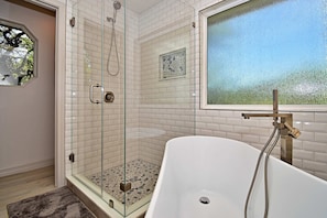 Un bagno moderno con cabina doccia in vetro, una vasca da bagno indipendente e una finestra vista alberi.