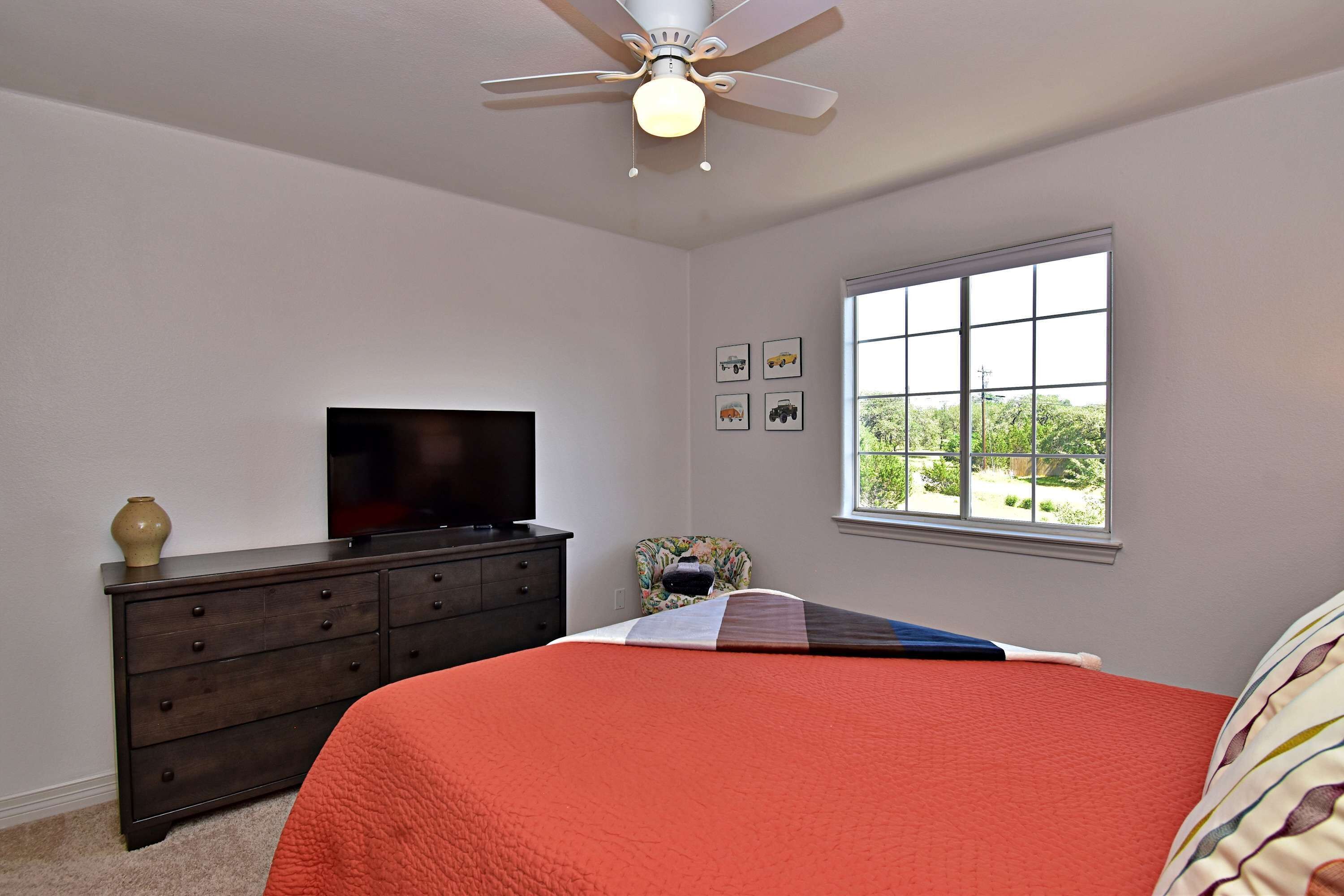 A bedroom with a bed, dresser, television, and window.