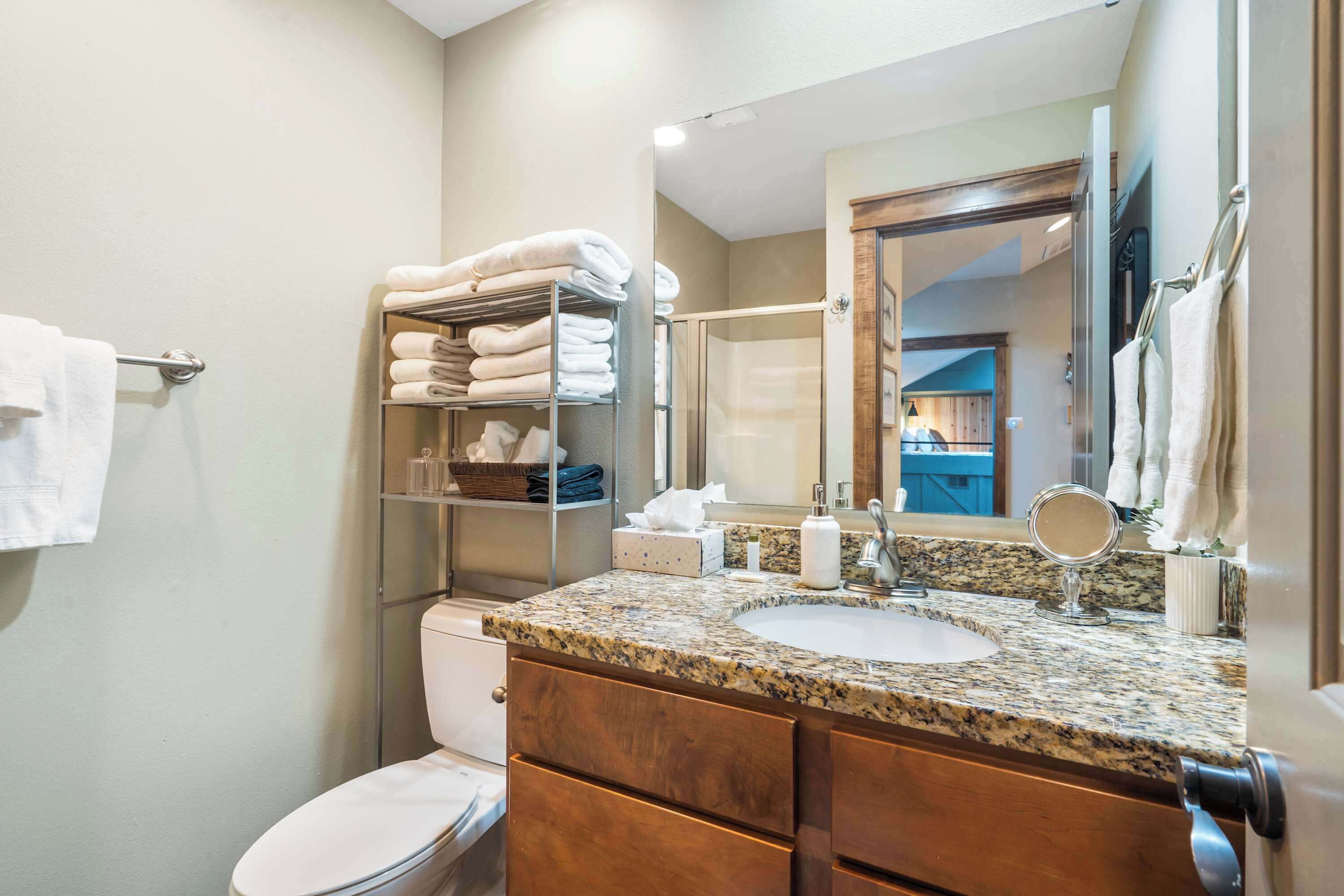 A bathroom with a granite countertop sink, a mirror, a toilet, and a towel rack.