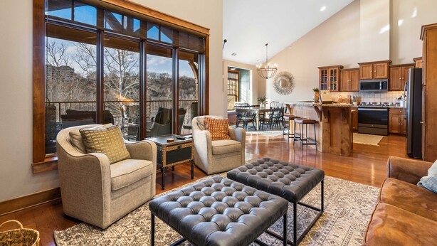 A spacious living area with a large window, a kitchen with wooden cabinets, and a dining area. - Penthouse 7 on Taneycomo - Chic Waterfront Condo! (Branson)