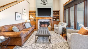 A cozy living room with a fireplace, leather sofa, and a television mounted above it. - Penthouse 7 on Taneycomo - Chic Waterfront Condo! (Branson)