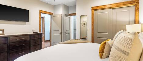 A bedroom with a large bed, a ceiling fan, a dresser, and a TV mounted on the wall.