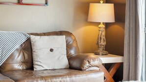 Ein braunes Ledersofa mit einem weißen Kissen und einer gestreiften Decke, ein Holznachttisch mit einer Lampe und ein Fenster mit Vorhängen.
