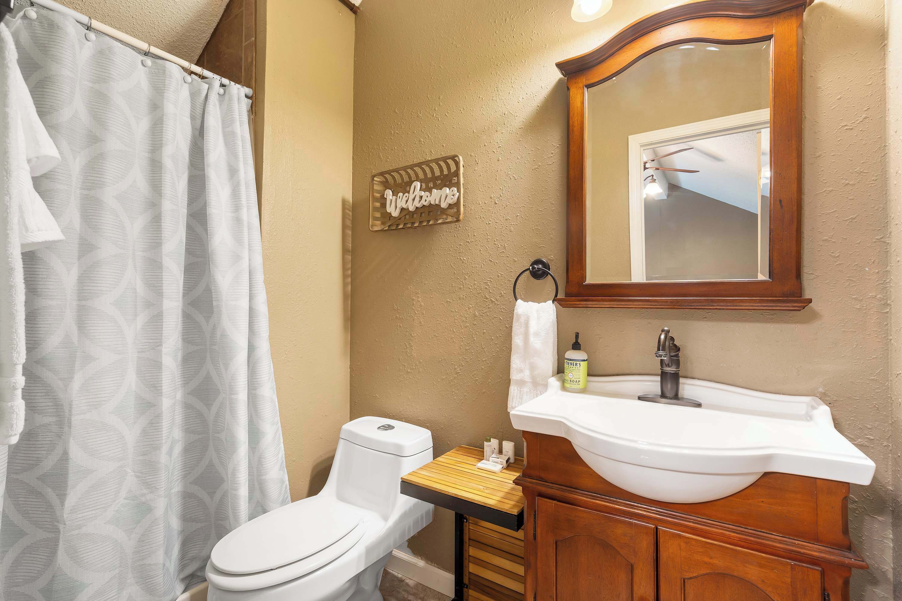 A bathroom with a toilet, a sink, a mirror, and a 'Welcome' sign.