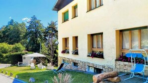 Un edificio a due piani con esterno chiaro, un piccolo giardino con prato e un patio in legno.