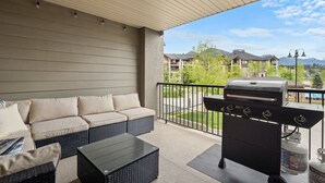 Een overdekt balkon met een barbecue, zitplaatsen buiten en uitzicht op een woonwijk.