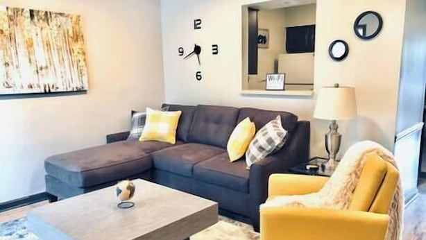 Un salon comprenant un canapé d’angle, un fauteuil jaune, une table basse et un tableau accroché au mur.
