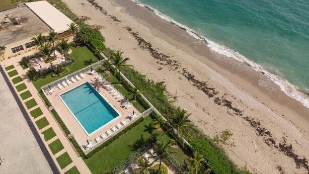 Vista aérea de uma propriedade à beira-mar com piscina, palmeiras e uma praia de areia.
