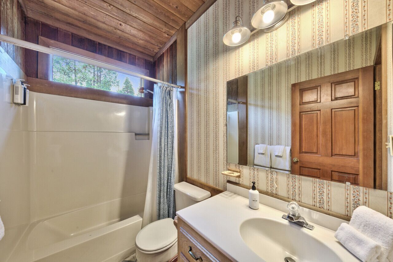 A bathroom with a wooden ceiling, a large mirror, a sink, and a toilet.