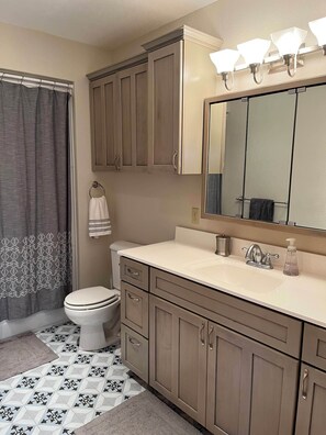 Un baño con inodoro, lavamanos, espejo y mueble de almacenamiento.