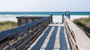 En træpromenade der fører til stranden med et sikkerhedsskilte.