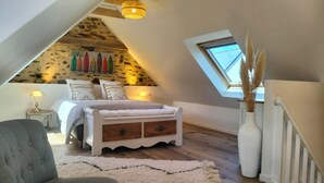 Une chambre avec un plafond en pente, un lit doté d’une tête de lit en bois, un radiateur blanc et un puits de lumière.