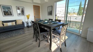 Un espace repas moderne avec une table en bois foncé, des chaises noires et une grande fenêtre donnant sur le paysage urbain.