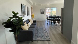 Un salon moderne avec un canapé gris foncé, une grande plante en pot et un tapis à motifs bleus.