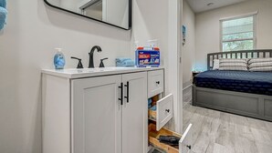 A modern bathroom with a white vanity, black faucets, and a mirror. There is a first aid kit on the vanity and a blue towel on the counter.
