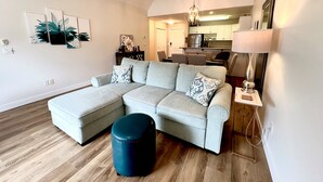 Una sala de estar moderna con un sofá modular, un otoman redondos y un comedor al fondo.