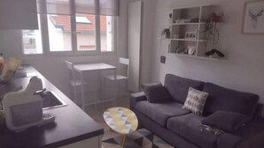 Ein Wohnzimmer mit einer Couch, einem kleinen runden Tisch und einer Küchenzeile mit einer Arbeitsplatte und Stühlen.