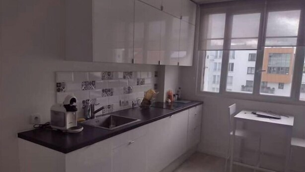 Eine moderne Küche mit weißen Schränken, einer schwarzen Arbeitsplatte und einem Fenster mit Blick auf Gebäude.