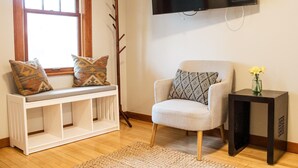 A living room with a bench, armchair, TV, and a small table with a vase. - Cute 2-bed home, 3 blocks from downtown Bozeman, with a large yard! (Bozeman)