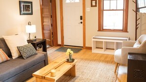 A living room with a sofa, a coffee table, a bench, and a TV stand. - Cute 2-bed home, 3 blocks from downtown Bozeman, with a large yard! (Bozeman)