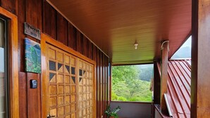 Un couloir en bois avec un sol carrelé, une porte décorative et une vue sur la verdure à l’extérieur.