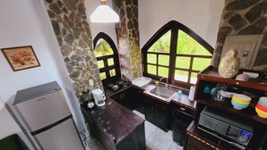 Une cuisine compacte avec un mur en pierre, un réfrigérateur, une machine à café, un évier et une cuisinière.