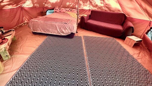Een tent met een bed, een rode bank en kamerbreed tapijt.