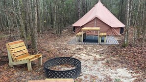 Een tent opgesteld in een bos, met een picknicktafel en bankjes in de buurt.