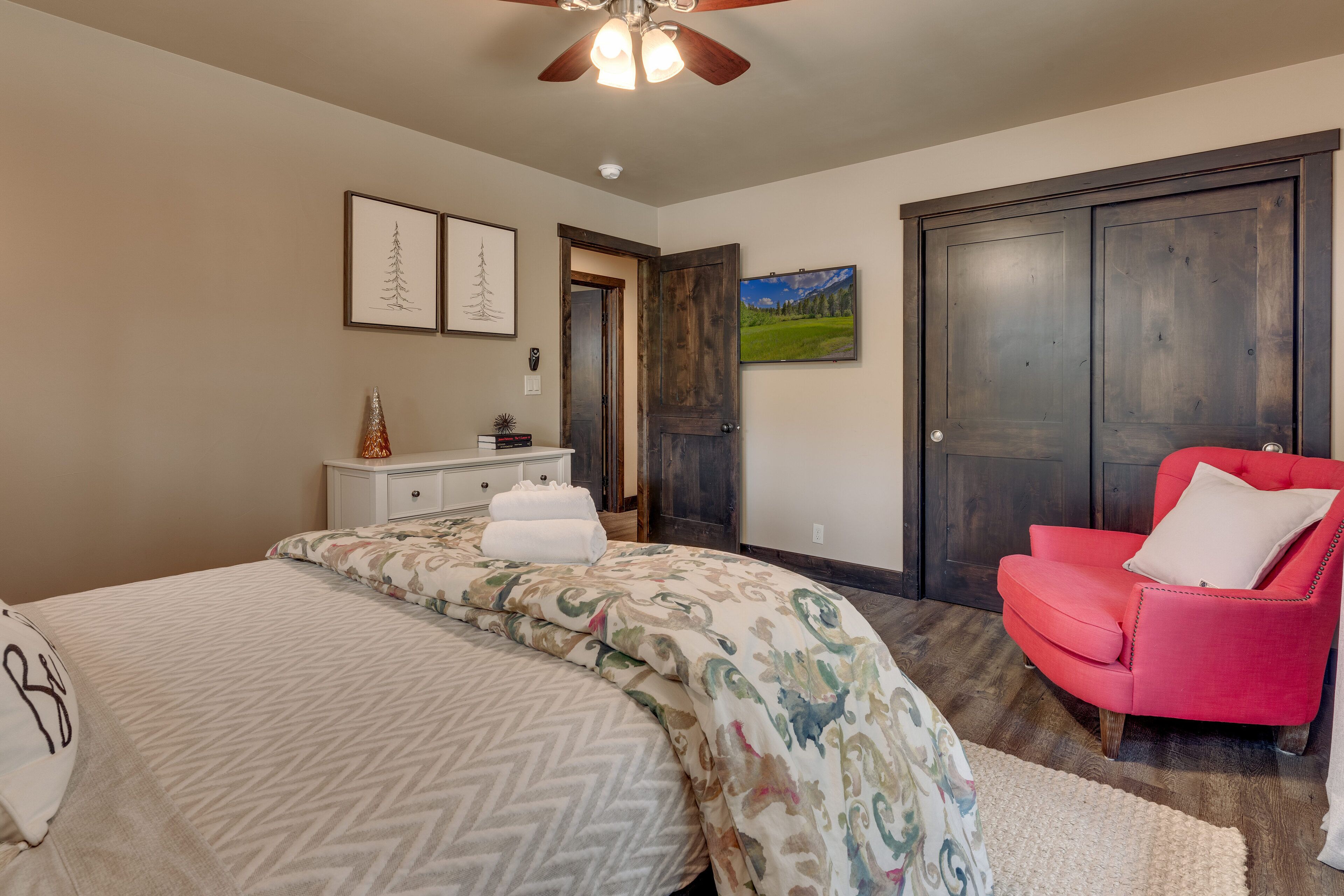 A bedroom with a bed, a red chair, a dresser, and a door.