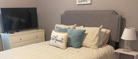 A neatly arranged bedroom with a large bed, a television on a dresser, and a motivational quote on the wall.