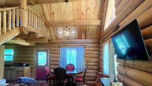 A log cabin interior with a dining area, seating, a fireplace, and a television. - Spring Pond Cabin at White Buffalo Lodge;
Family-sized with lake access (Grove)